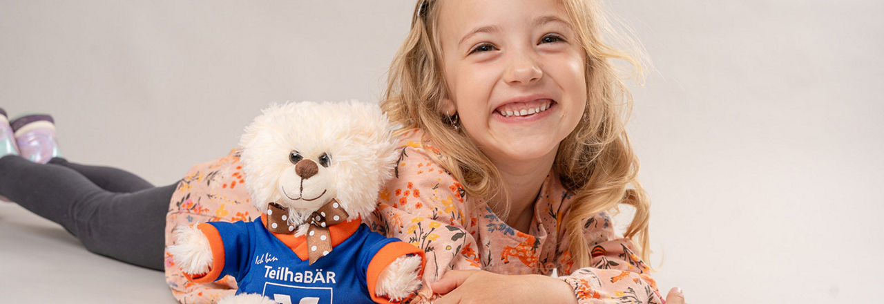 Kind mit Teddy neben sich lächelt