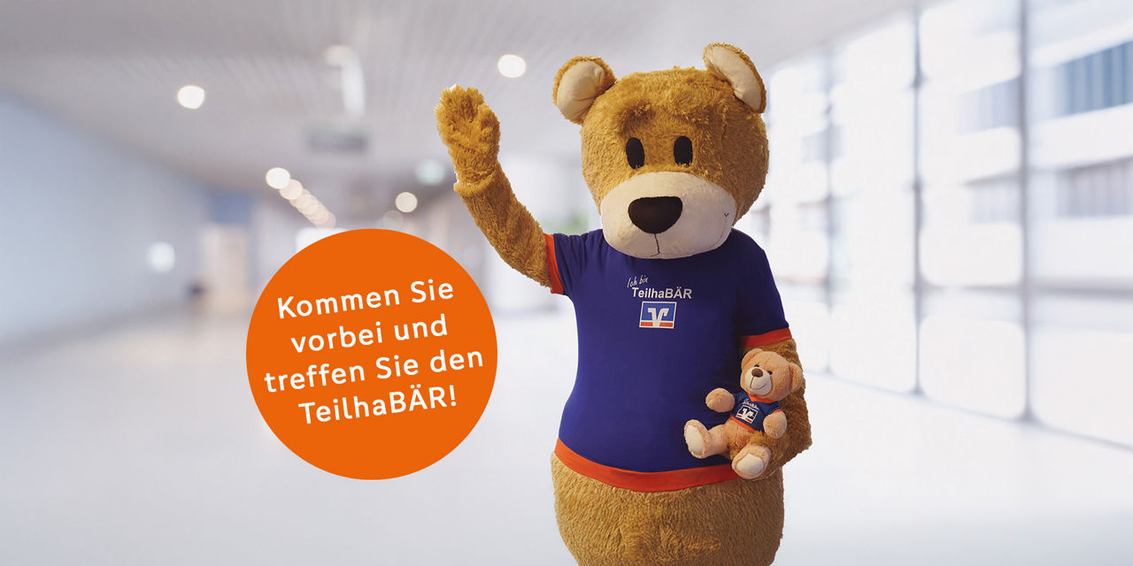 Der ,,Teilhabär" (Bärenkostüm der Volksbank Mittlerer Neckar eG) hat einen Plüschteddy in der Hand und winkt in die Kamera.