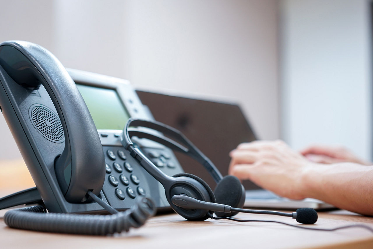 Telefon, Headset und Laptop. Hände des Call-Center Mitarbeiters liegen auf der Tastatur.