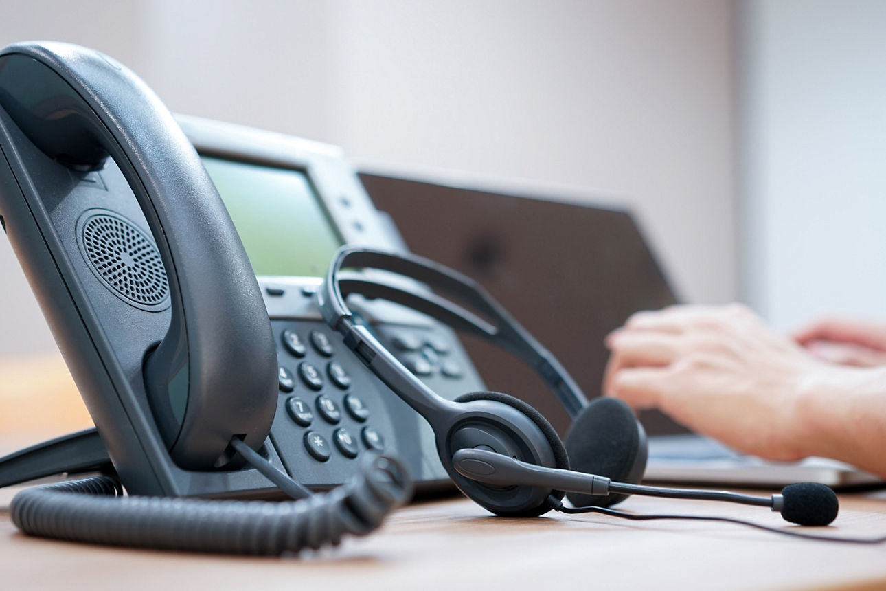 Telefon, Headset und Laptop. Hände des Call-Center Mitarbeiters liegen auf der Tastatur.