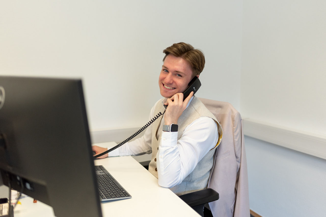 Junger Mann sitzt mit Telefonhörer in der Hand vor Computerbildschirmen