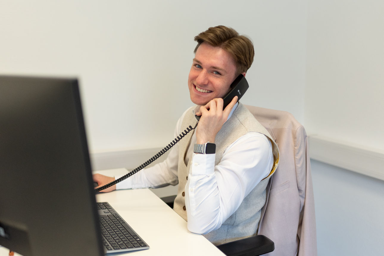 Junger Mann sitzt mit Telefonhörer in der Hand vor Computerbildschirmen