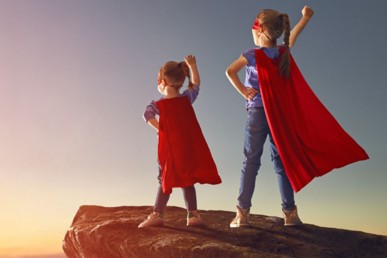 Zwei Kinder in Superheldenkostümen stehen auf einem Felsen mit Blick in den Sonnenuntergang – daneben eine Sprechblase mit dem Text: ‚Termingeld für Minderjährige.