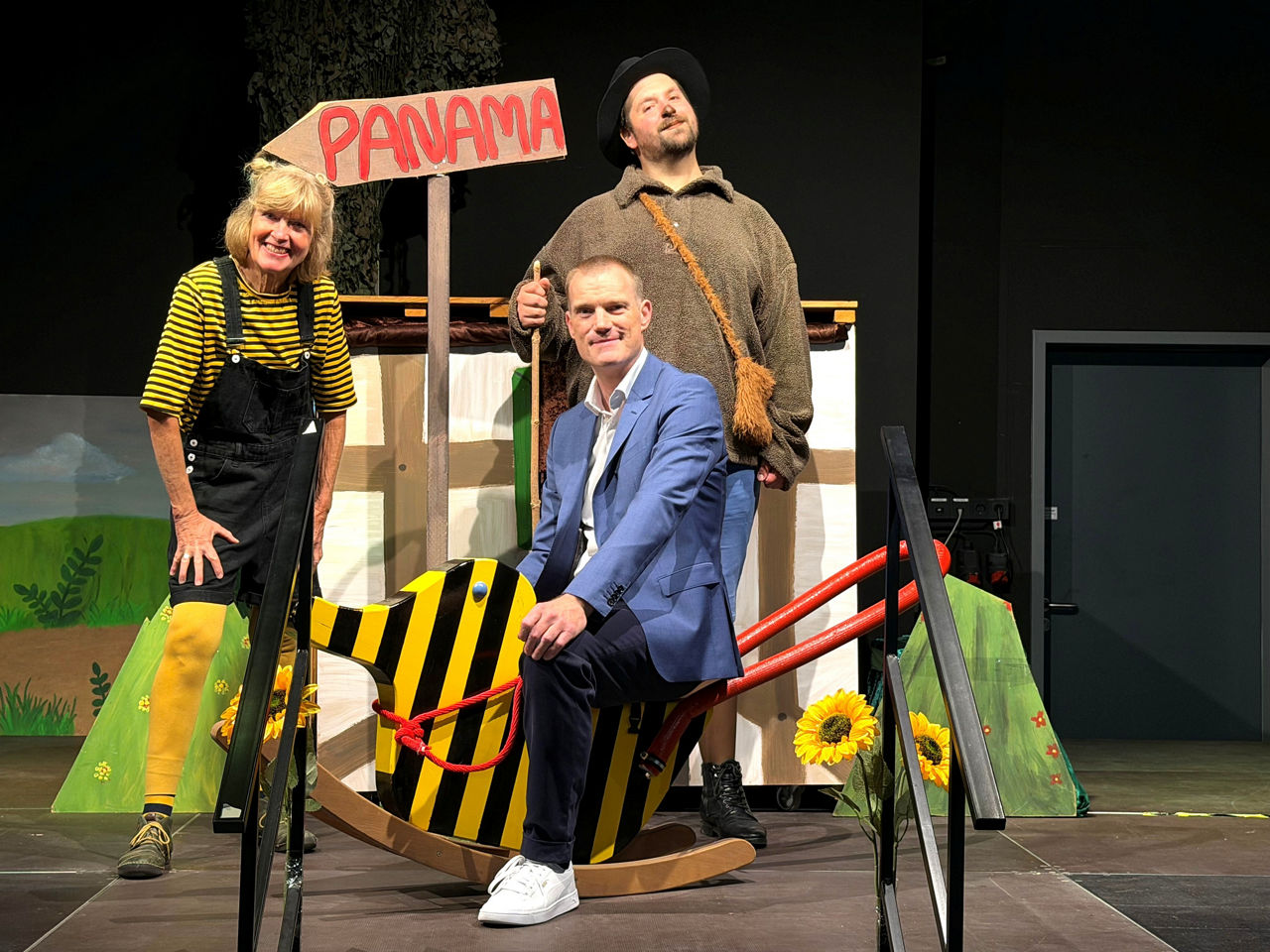 Regionalleiter der VerbundVolksbank OWL eG mit zwei Mitwirkenden vom Theater Exil auf der Bühne mit Requisiten.    