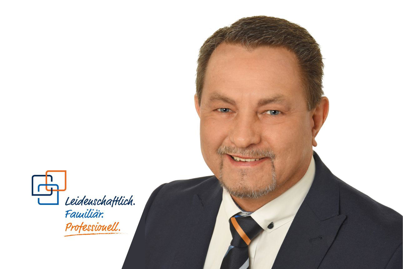 Porträt von Thomas Reichlmayr, einem lächelnden Mann mit kurzen dunklen Haaren und Bart im dunklen Anzug mit weißem Hemd und gestreifter Krawatte. Daneben das Firmenlogo und der Slogan "Leidenschaftlich. Familiär. Professionell."