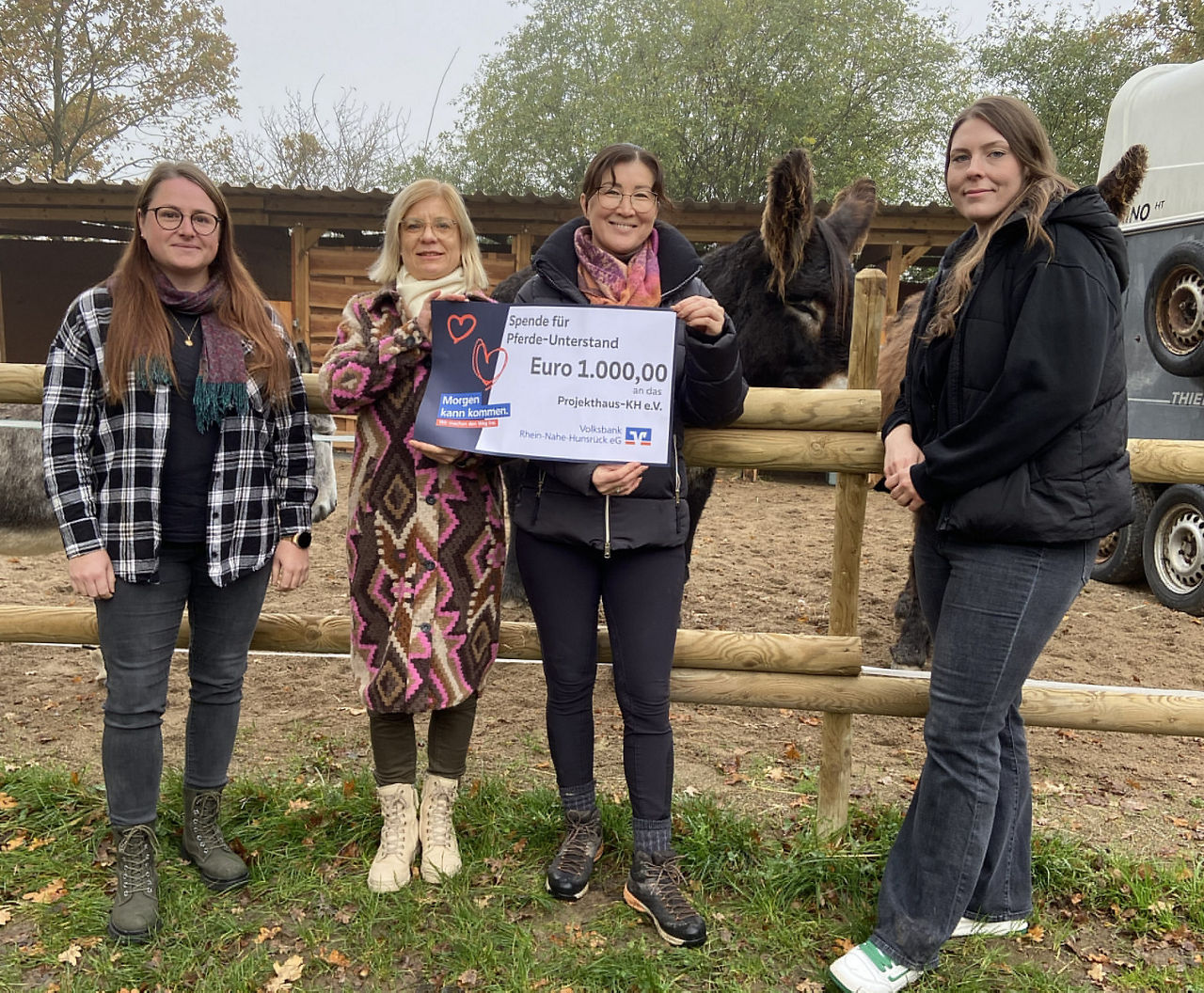 Zwei Erwachsene halten den Spendenscheck in der Hand und stehen vor einem Zaun.