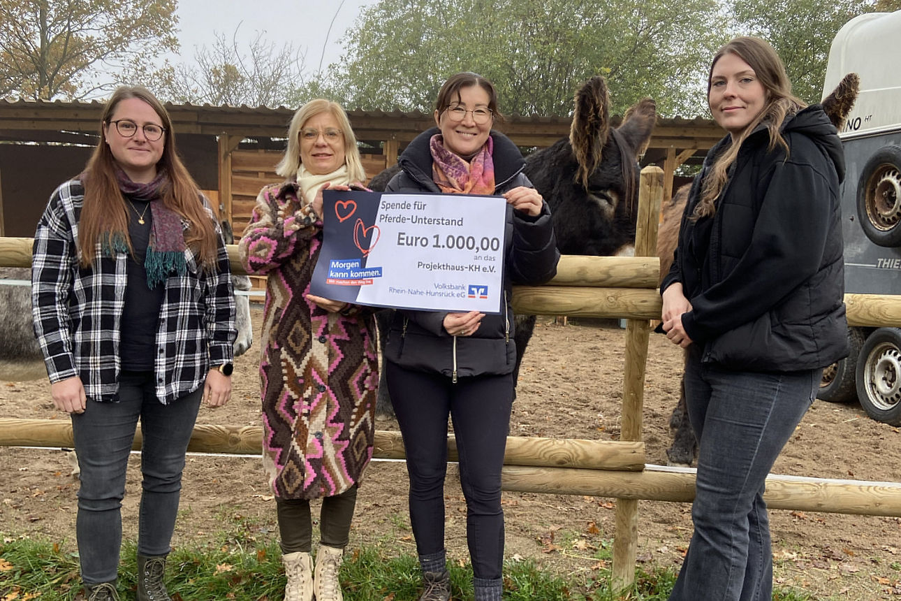 Zwei Erwachsene halten den Spendenscheck in der Hand und stehen vor einem Zaun.