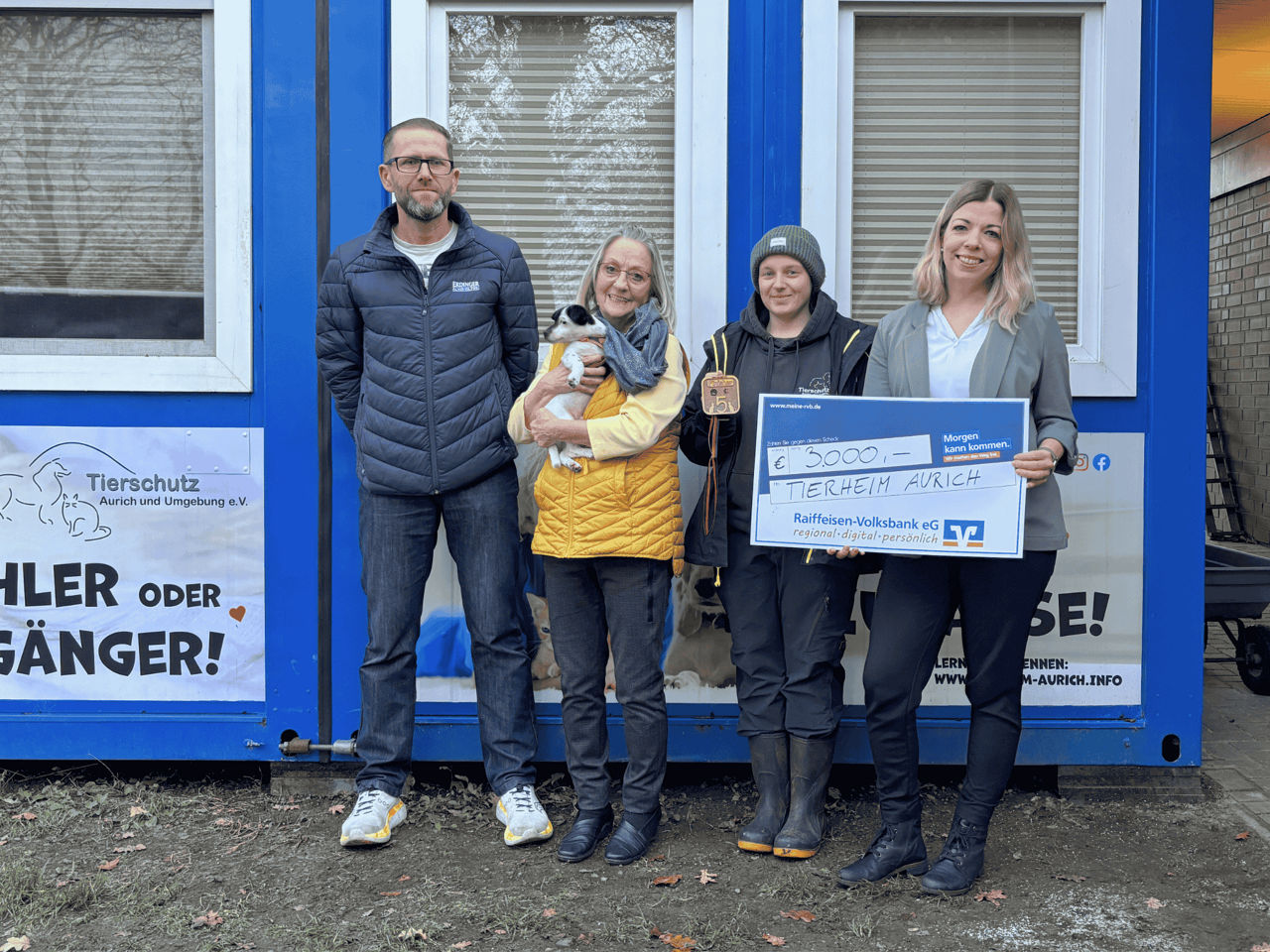 Vier Personen und ein Hund bei einer symbolischen Scheckübergabe 