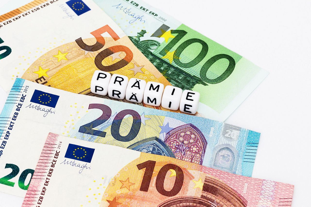 Geldscheine auf denen Würfel liegen die das Wort PRÄMIE zeigen
