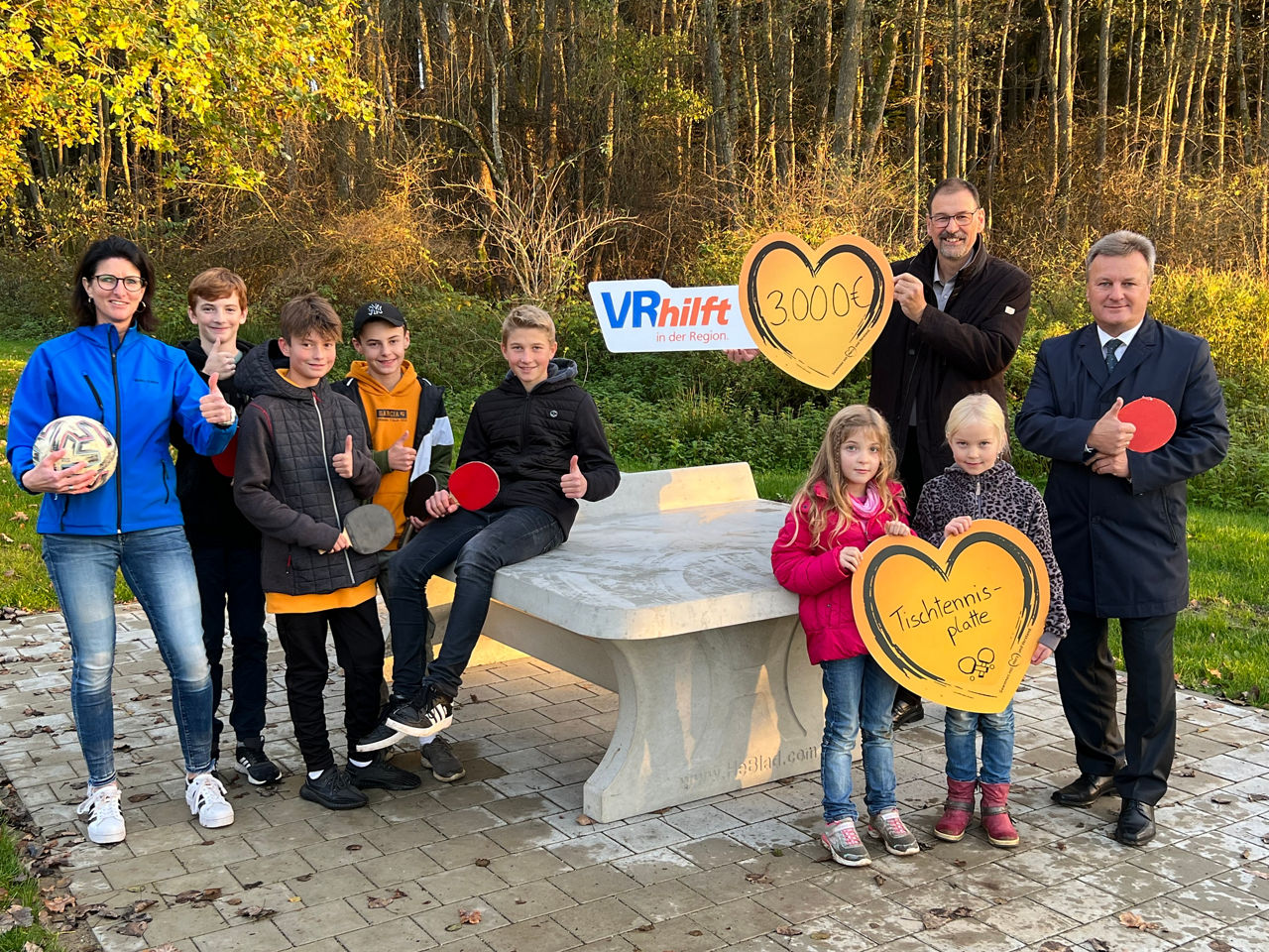 Foto von Kindern und Erwachsenen, die sich an einer Tischtennisplatte aus Beton in der Natur vergnügen