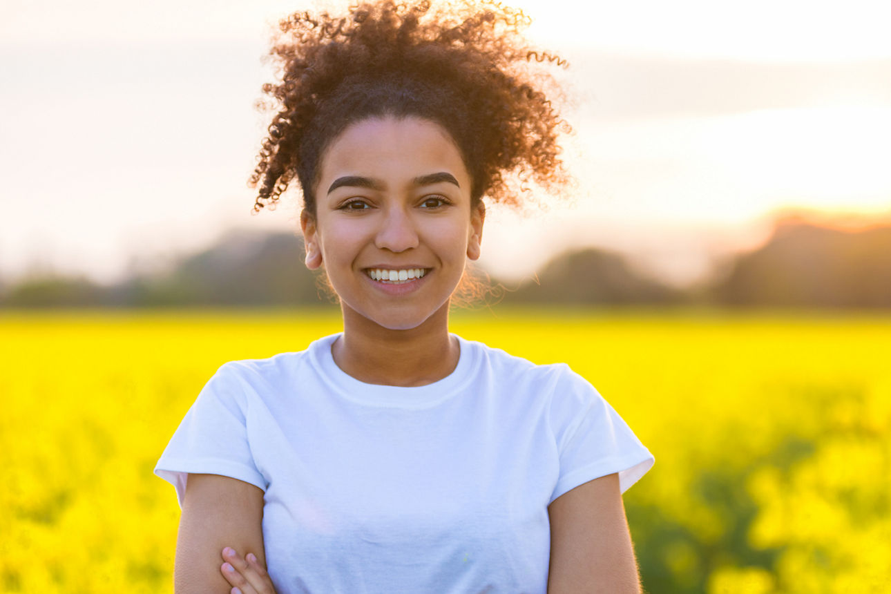 Frau steht im Rapsfeld und lacht in die Kamera