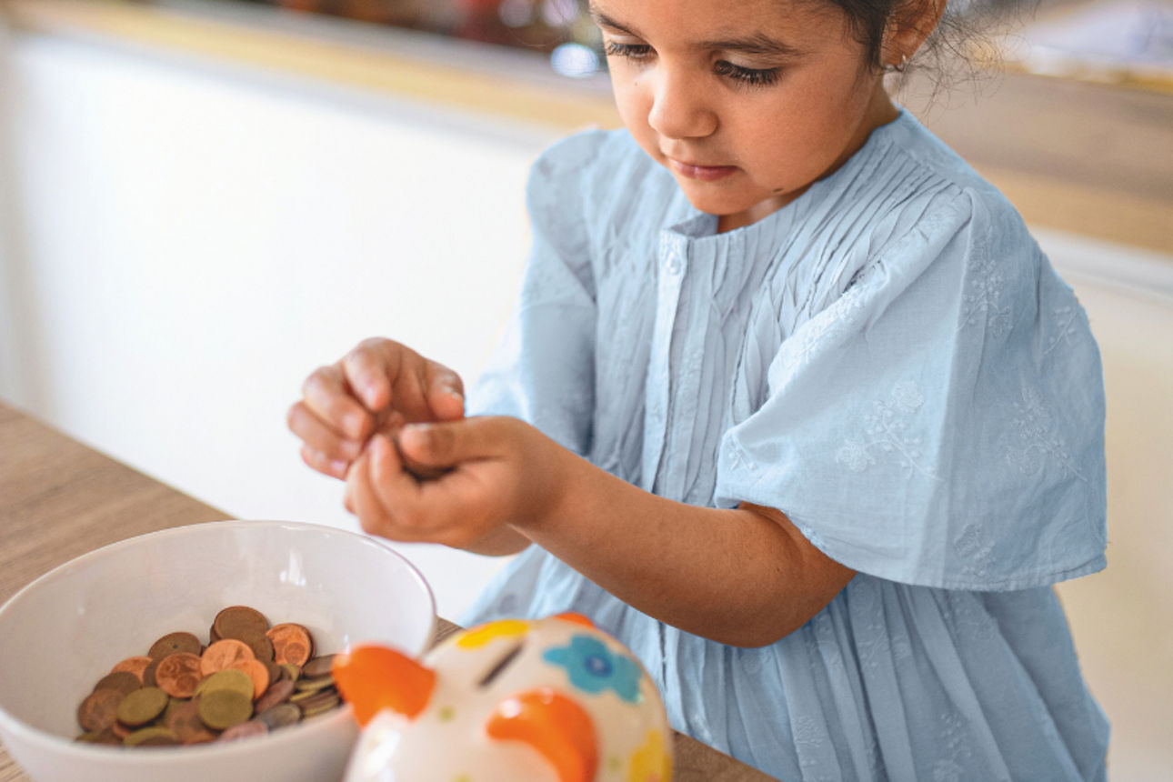 Ein Kind zählt Münzen am Küchentisch und legt sie in eine Sparschale – ein Motiv für Sparen und den Umgang mit Geld.