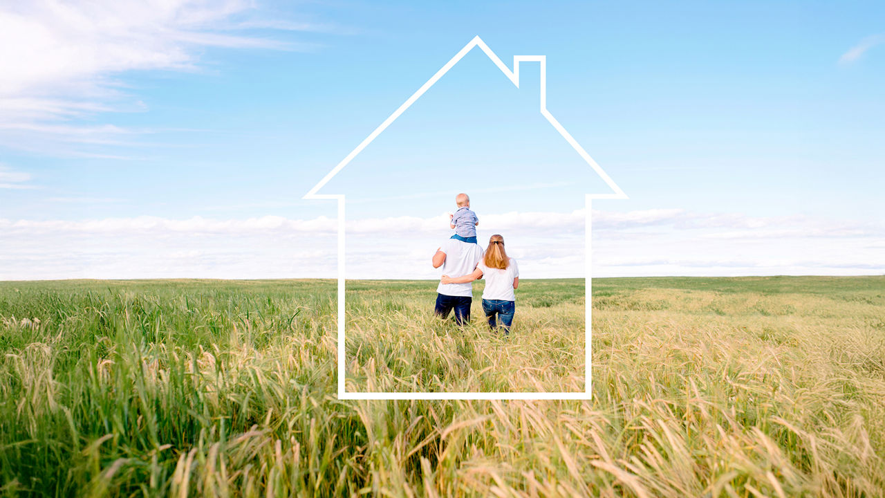 Familie steht in einer Graslandschaft und wird von einem Rahmen in Haus-Form umfasst
