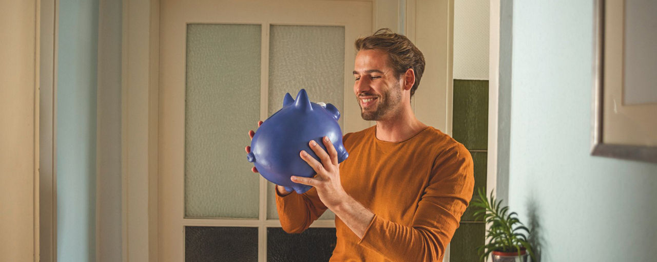 Mann schaut sein blaues Sparschwein an