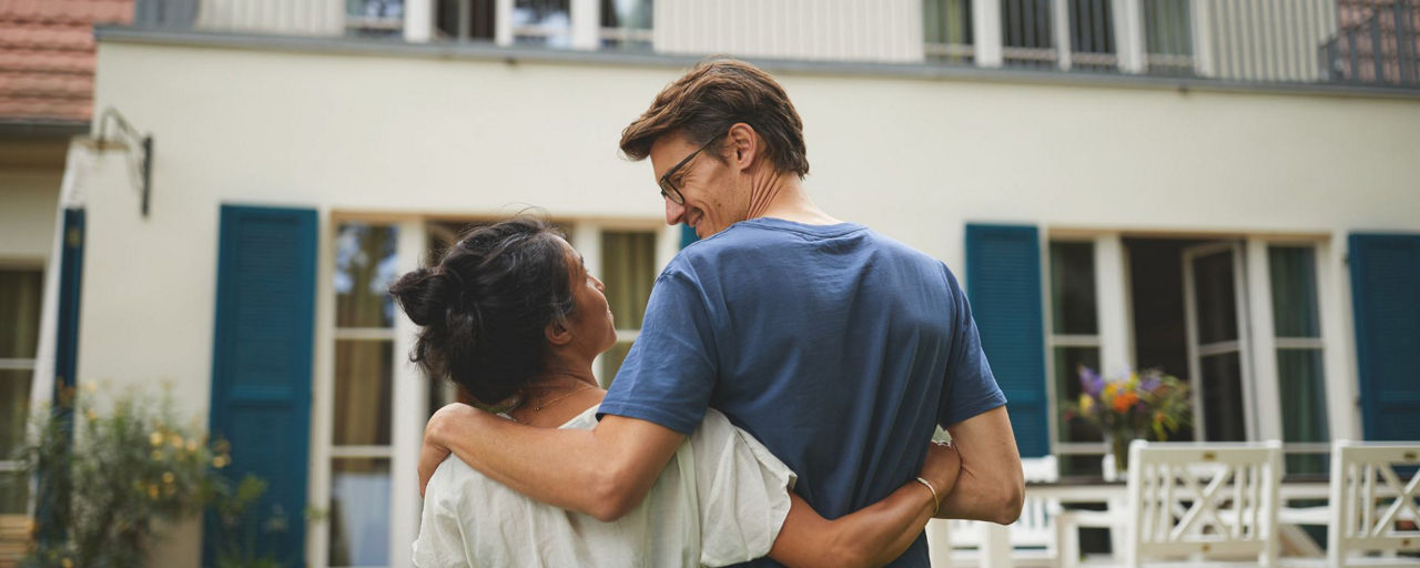 Mann und Frau halten sich vor einem Haus im Arm