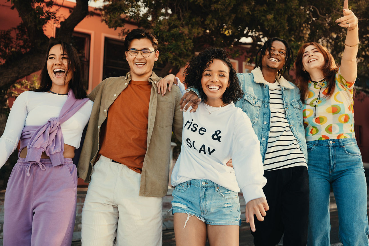 Eine Gruppe Jugendlicher steht eng beieinander, hält sich freundschaftlich im Arm und lacht ausgelassen