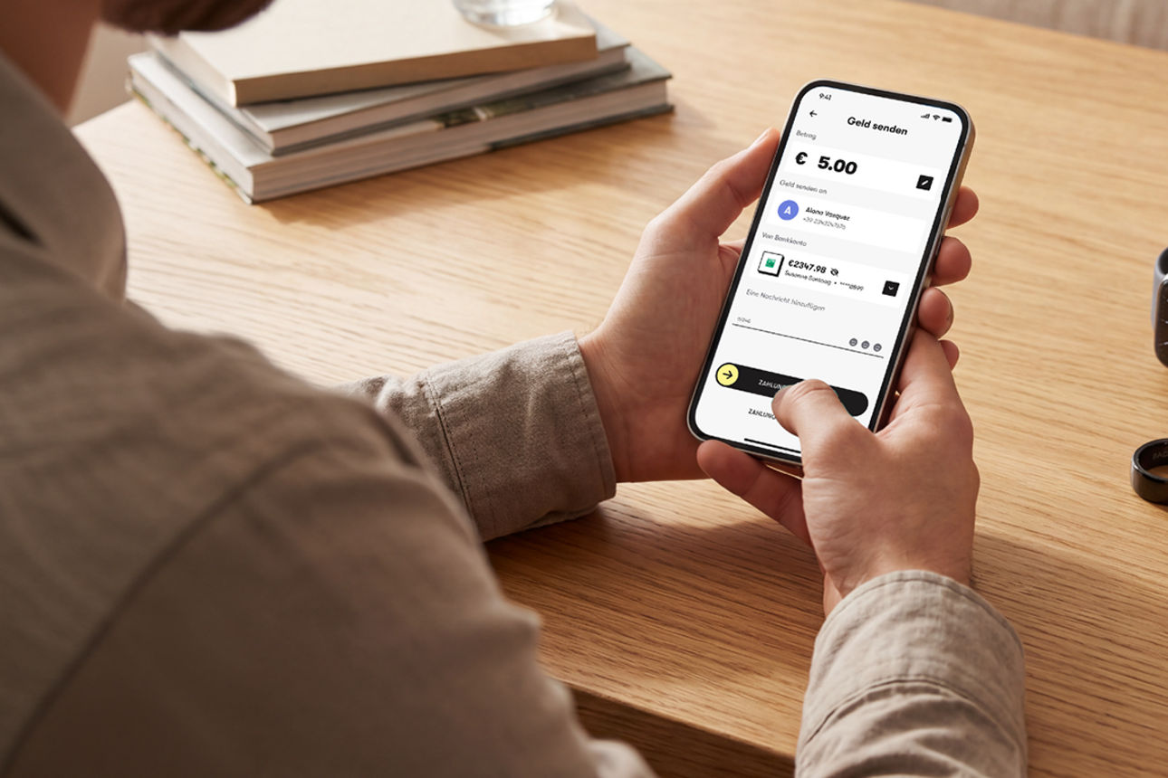 Mann hält ein Smartphone mit Wero am Wohnzimmertisch