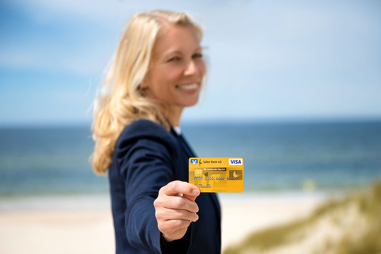 Eine Frau hält eine goldene Kreditkarte am Strand in die Kamera