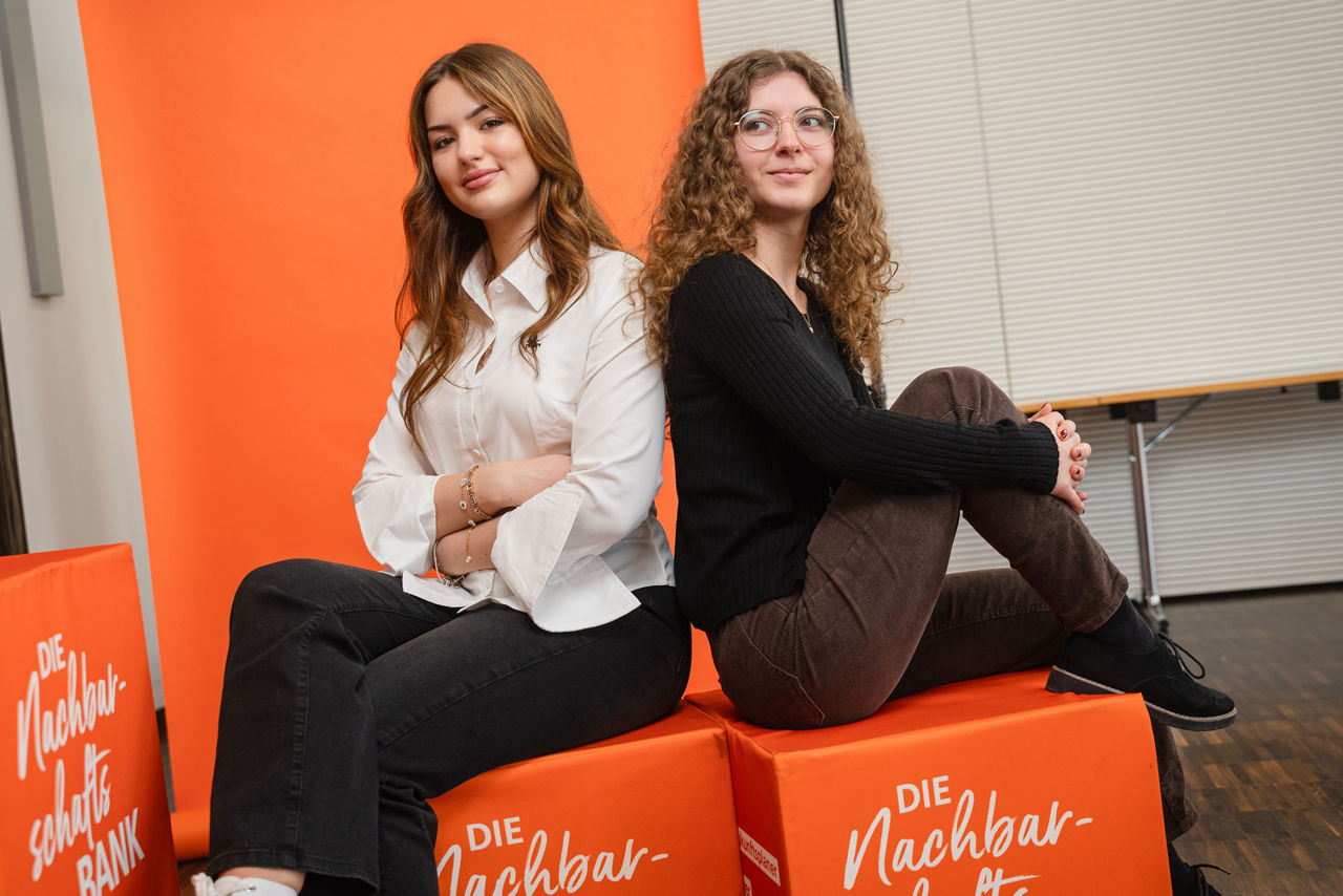Zwei junge Frauen sitzen auf orangenen Würfeln