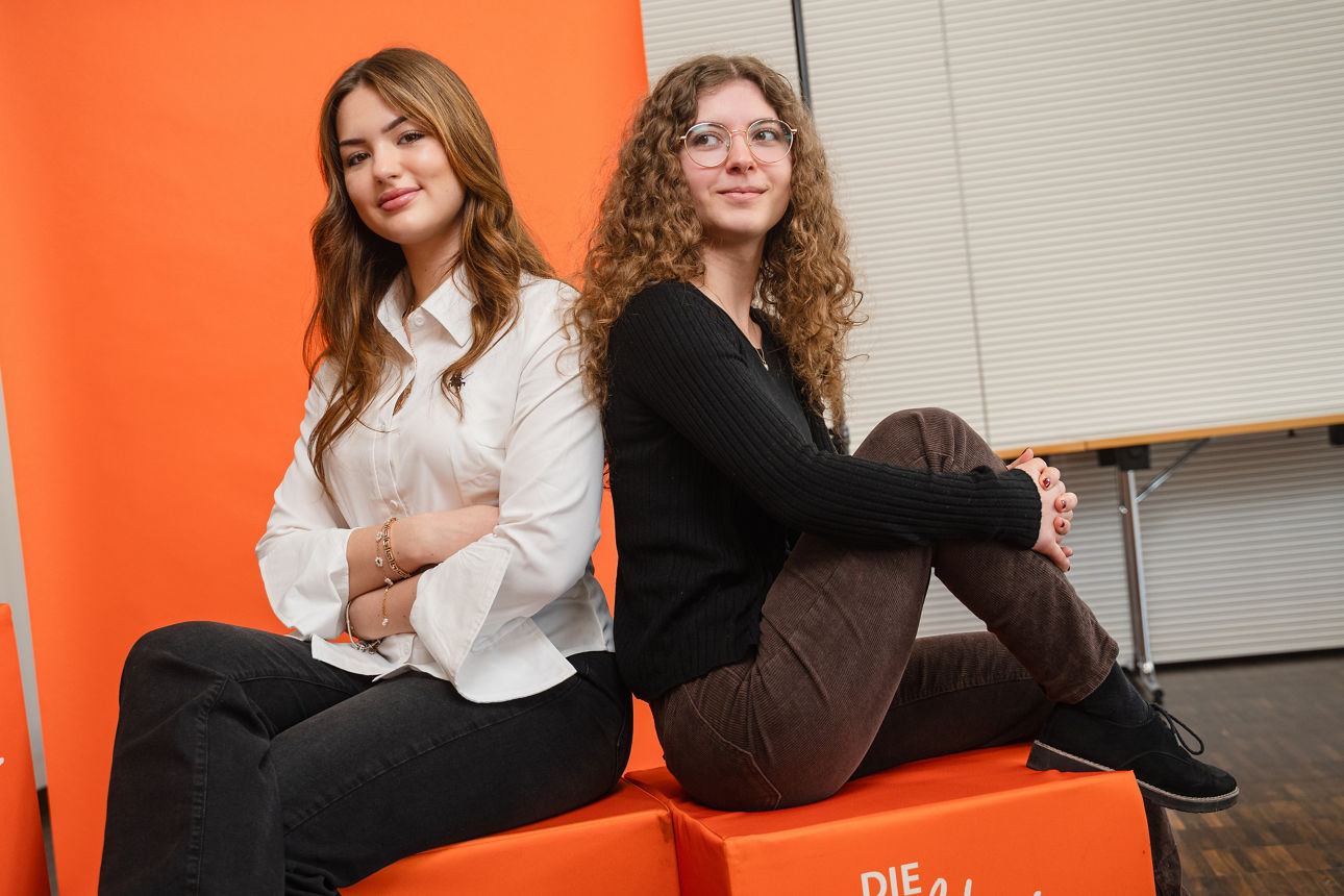 Zwei junge Frauen sitzen auf orangenen Würfeln