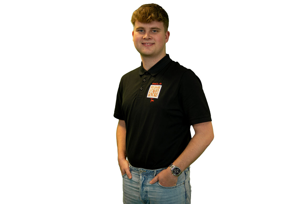 Junger Berufstätiger in einem schwarzen Poloshirt, hellen Jeans und einer Armbanduhr.