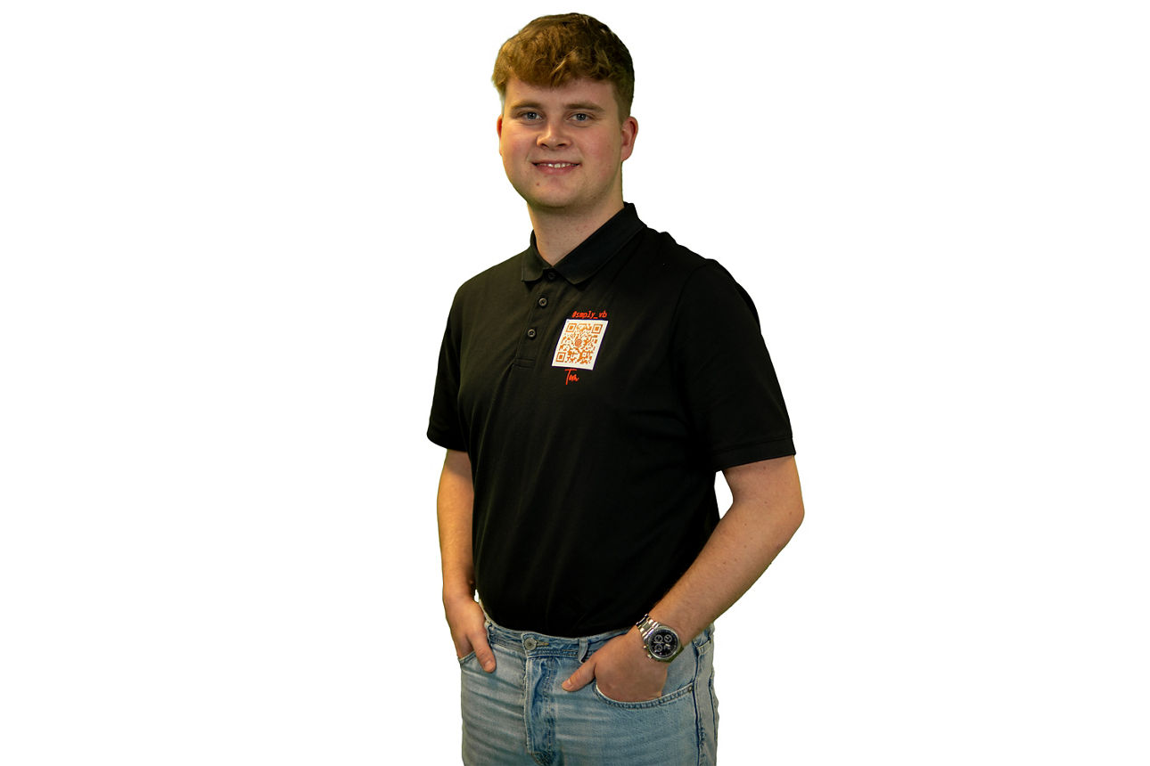Junger Berufstätiger in einem schwarzen Poloshirt, hellen Jeans und einer Armbanduhr.