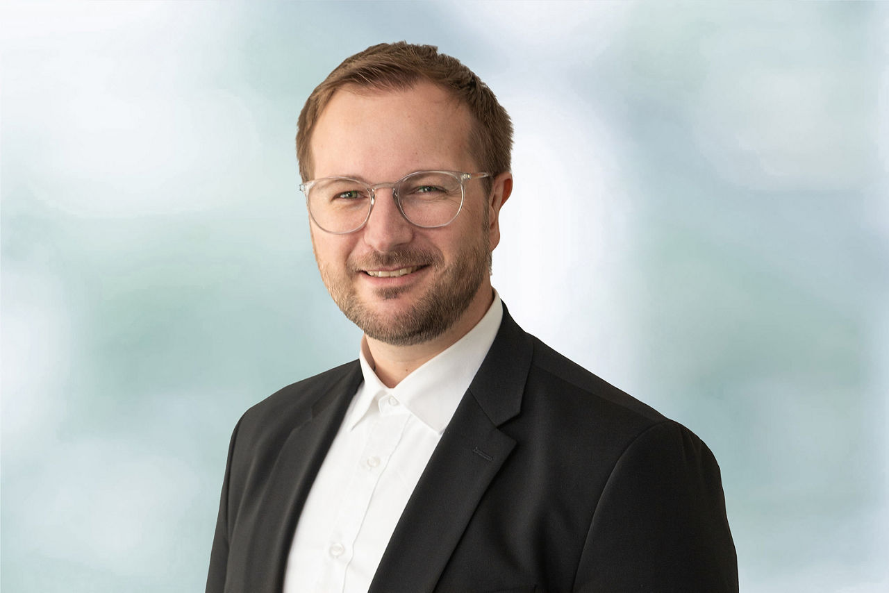 Ein sympathisch lächelnder Mann im Anzug, ohne Krawatte Anfang 30. Bei dem Mann handelt es sich um den Firmenkundenberater Christopher Topfmeyer.