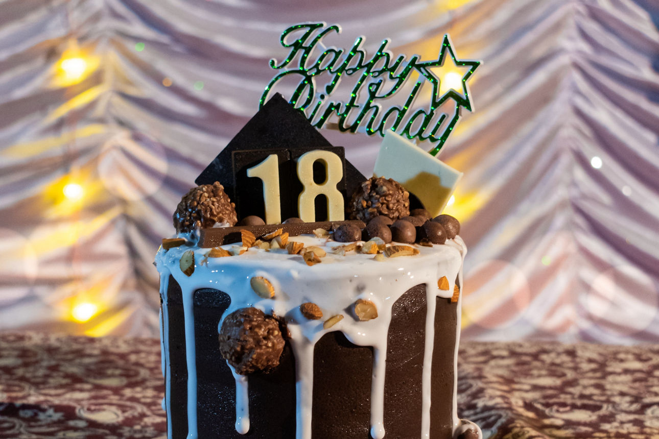 Dunkle Schokoladentorte mit „Happy Birthday“ und der Zahl 18, dekoriert mit Süßigkeiten.