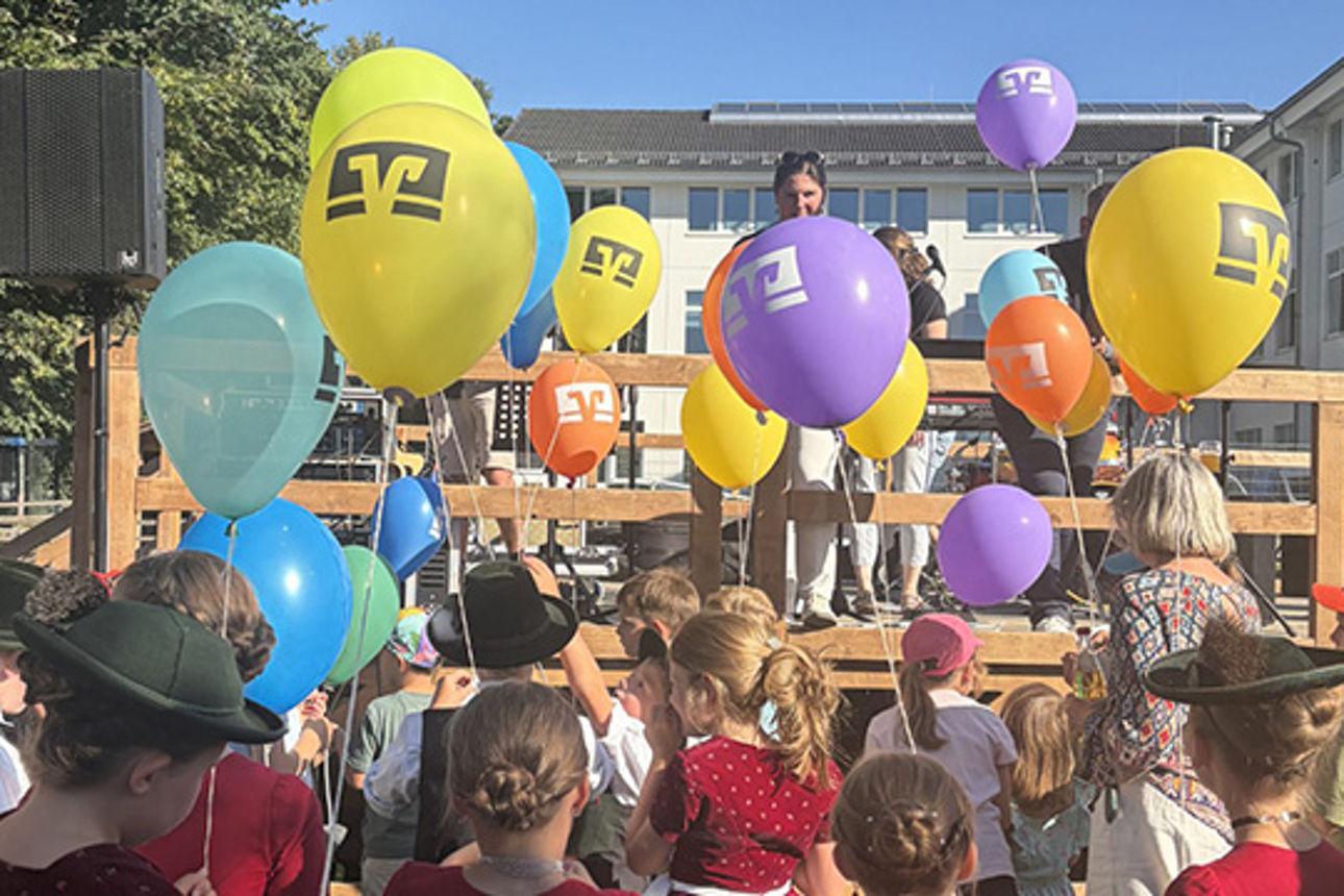 Kinder stehen mit Luftballonen in der Hand vor einer Bühne.
