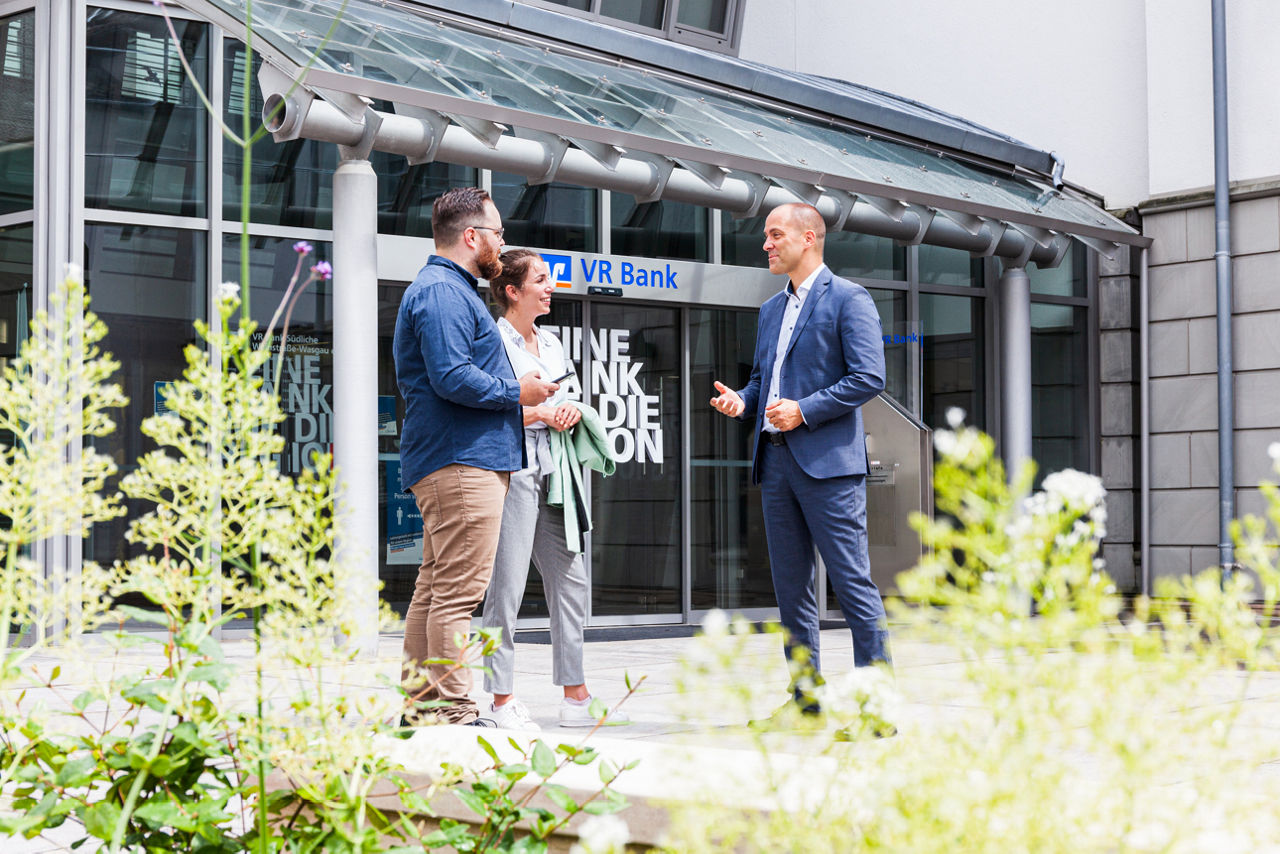 Berater mit Kunden im Gespräch vorm Eingang der Bank.
