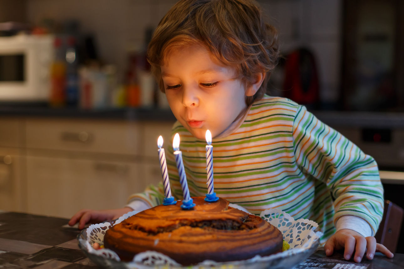 Kind beugt sich über einen Kuchen und bläst drei brennende Kerzen aus; Logos von Union Investment und VR Bank sichtbar.