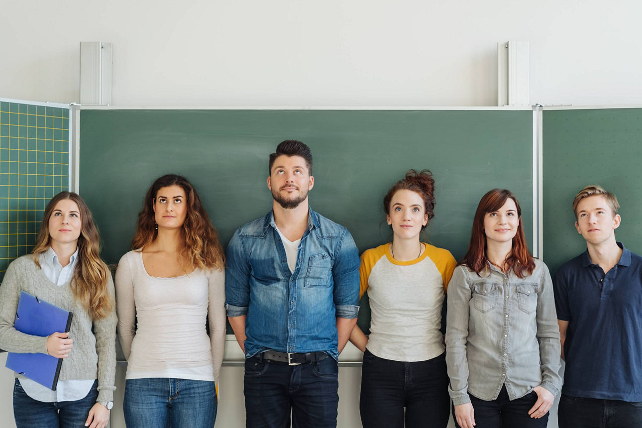Eine Gruppe Teilnehmende eines Traineeprogramms stehen vor einer Schultafel und symbolisieren Lernen, Weiterbildung und Berufseinstieg.