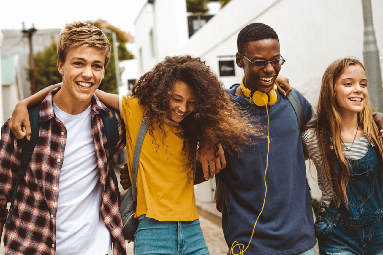 Vier junge Menschen laufen Arm-in-Arm eine Straße entlang