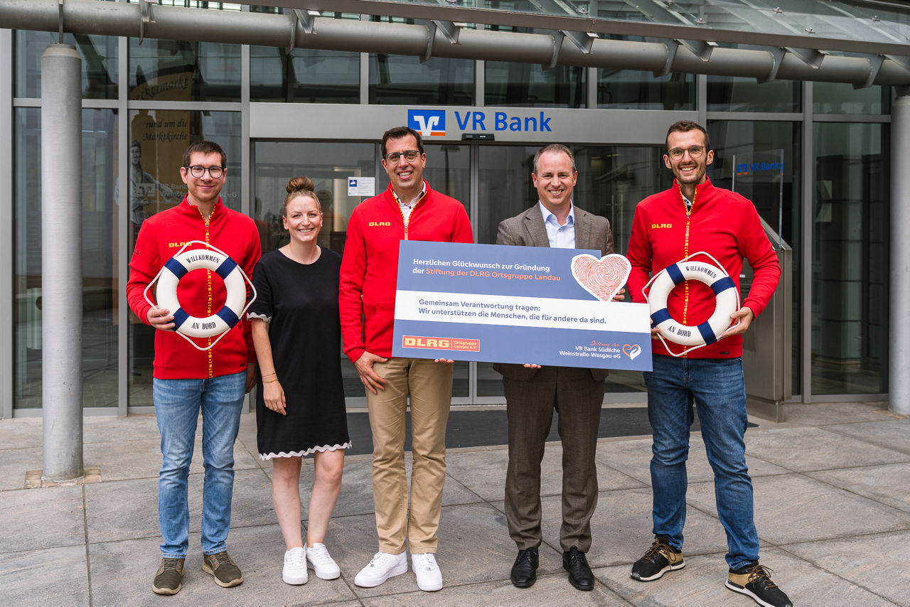 Gruppenfoto vor einer VR-Bank-Filiale mit DLRG-Mitgliedern, symbolischem Scheck und Rettungsringen