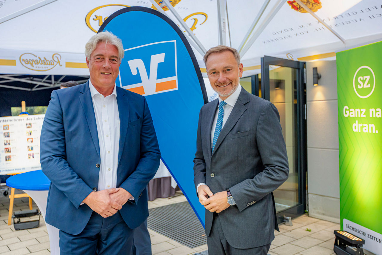 Zwei Männer lächeln in die Kamera vor Volksbank-Beachflag