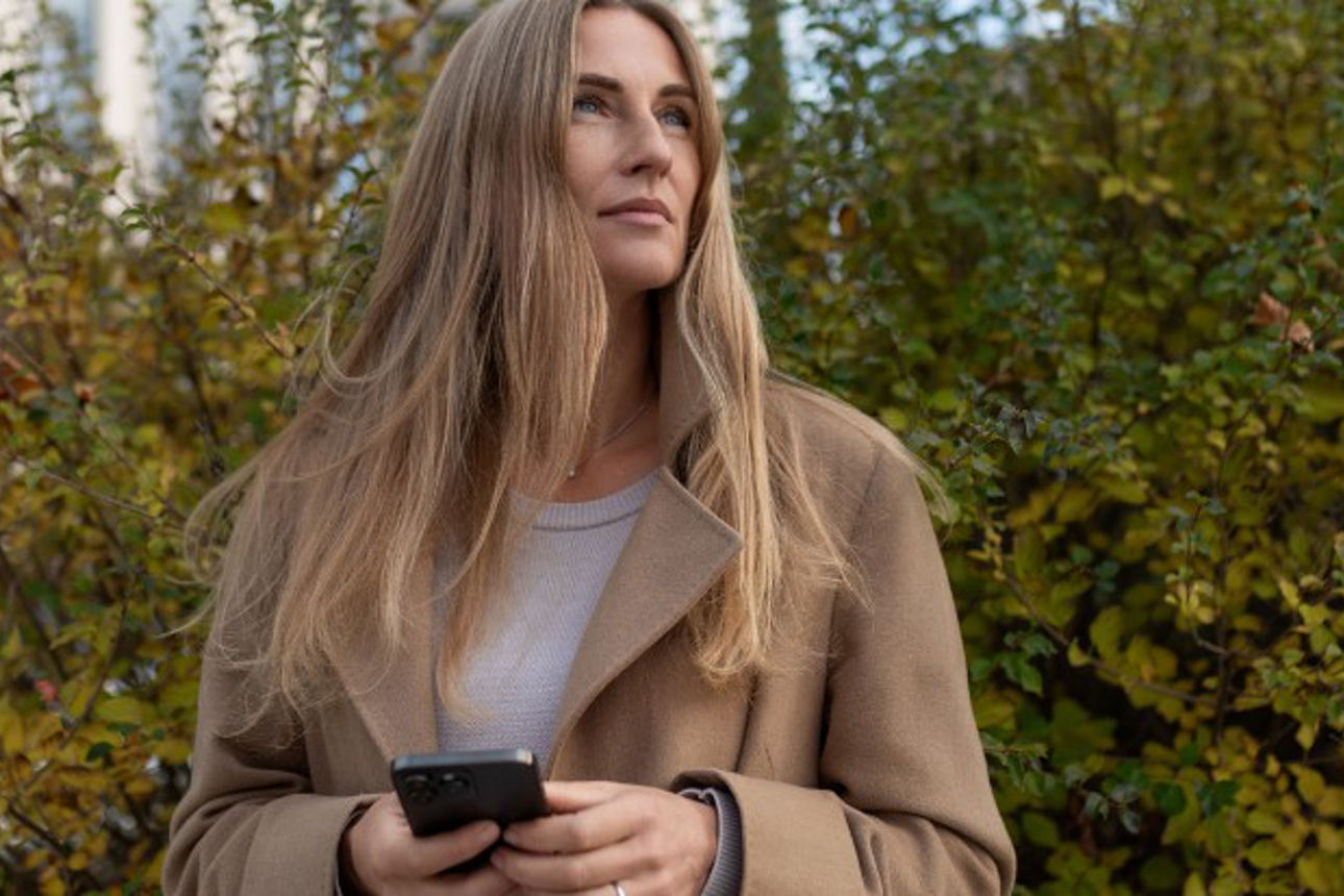 Frau steht vor einer Hecke und hält ein Handy in ihrer Hand