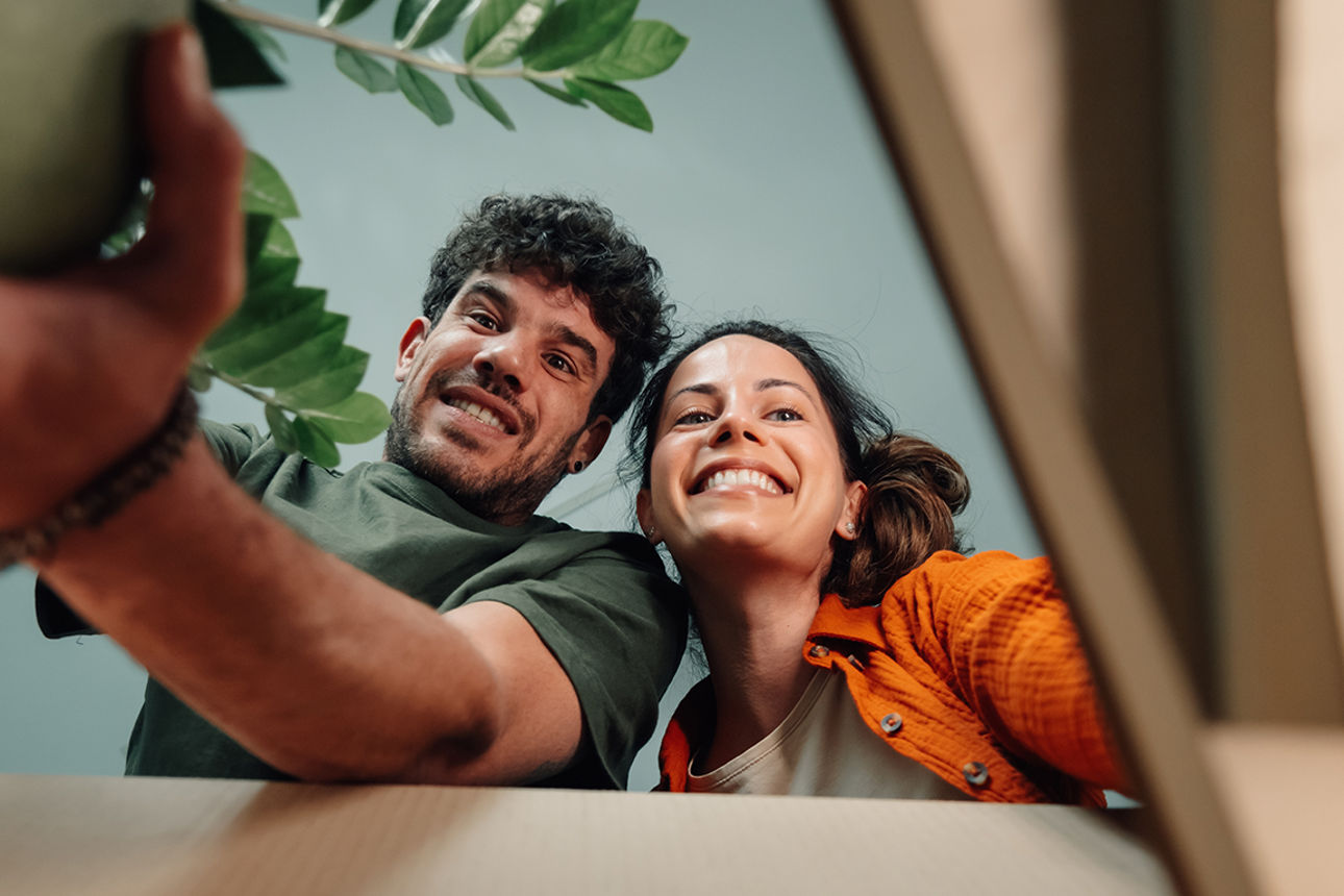 Ein Pärchen beugt sich über einen Umzugskarton und packt ihn aus.