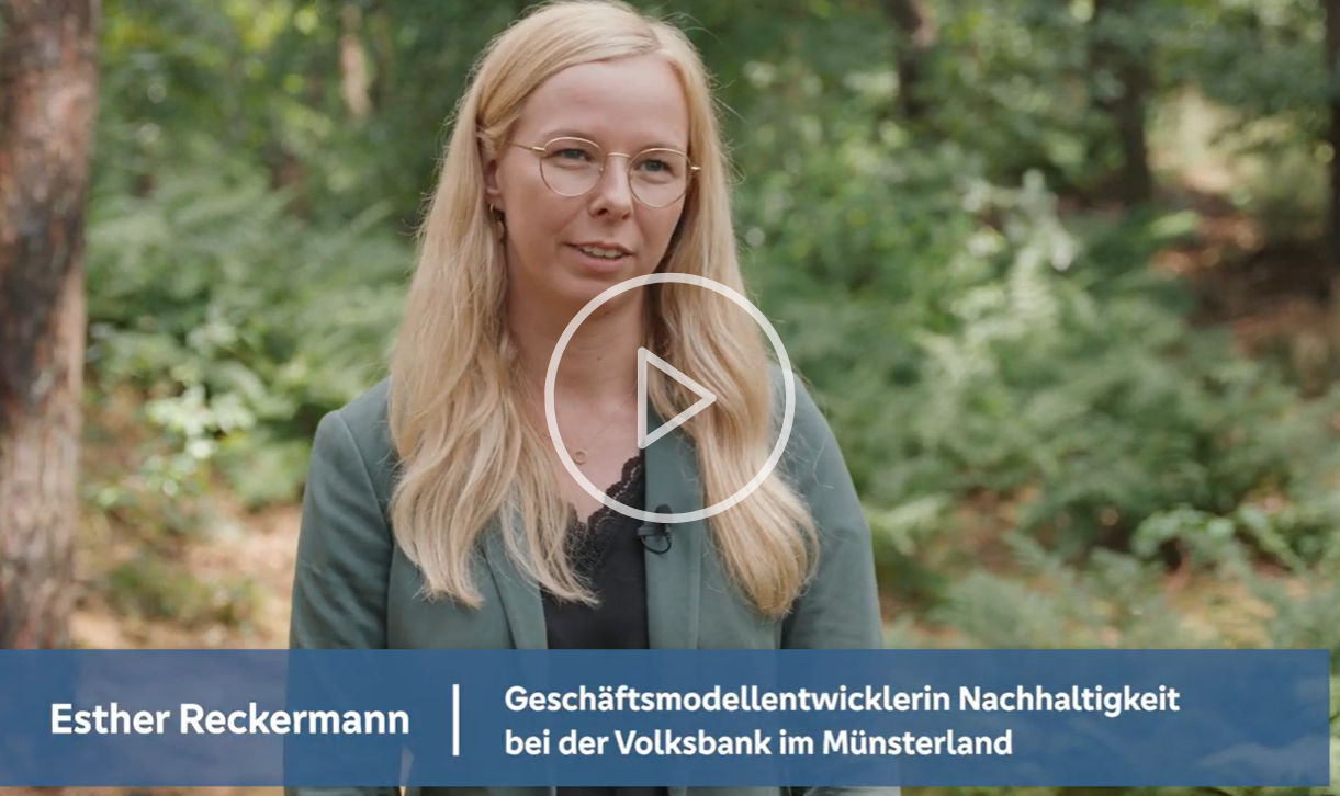 Eine Frau steht lächelnd im Wald und blickt in die Kamera.