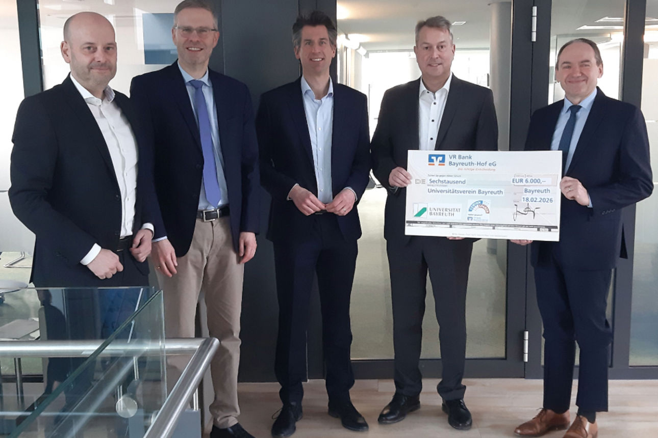 Fünf Personen stehen zusammen und halten einen großen symbolischen Spendenscheck in den Händen.