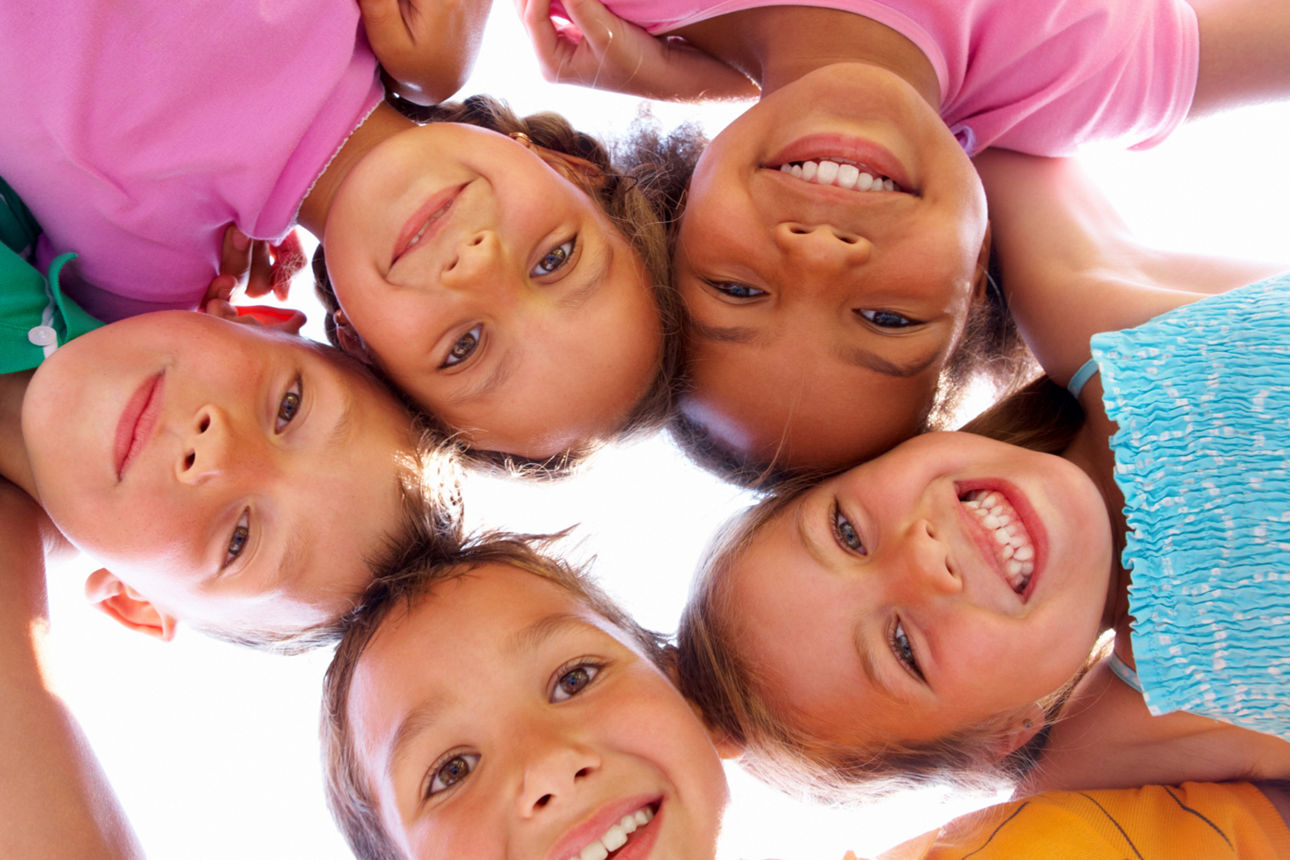 5 Kinder in bunten T-Shirts blicken nach unten in die Kamera und bilden dabei einen Kreis