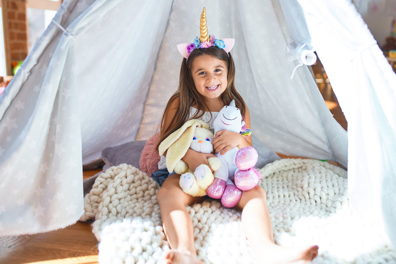 Entzückende Kleinkind sitzt auf dem Boden im Tipi um viele Spielzeuge im Kindergarten