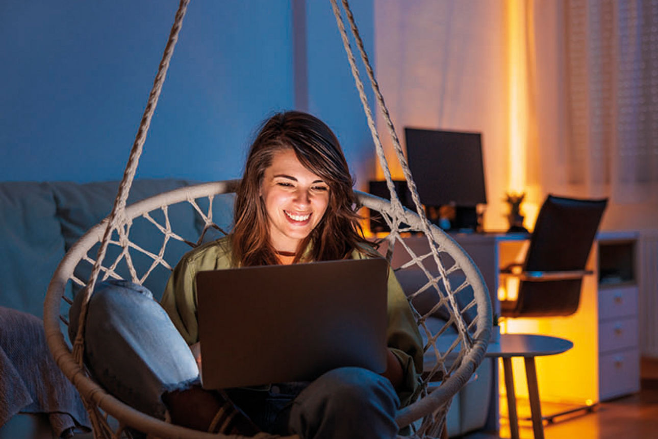 Junge Frau sitzt mit Notebook auf dem Bein in einer Hängeschaukel