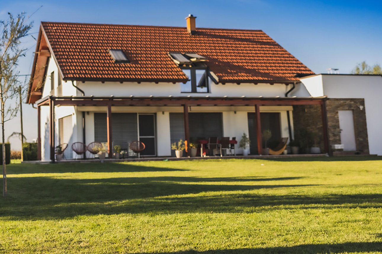 Ein Paar steht vor einem Haus. Sie sind von hinten zu sehen. Sie stehen auf einer großen Wiese vor dem Haus