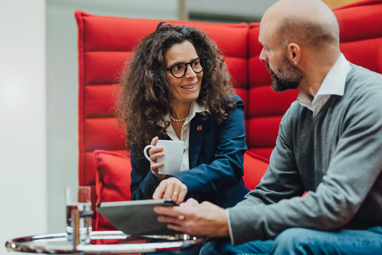 Zwei Personen sitzen auf einer roten Couch und unterhalten sich