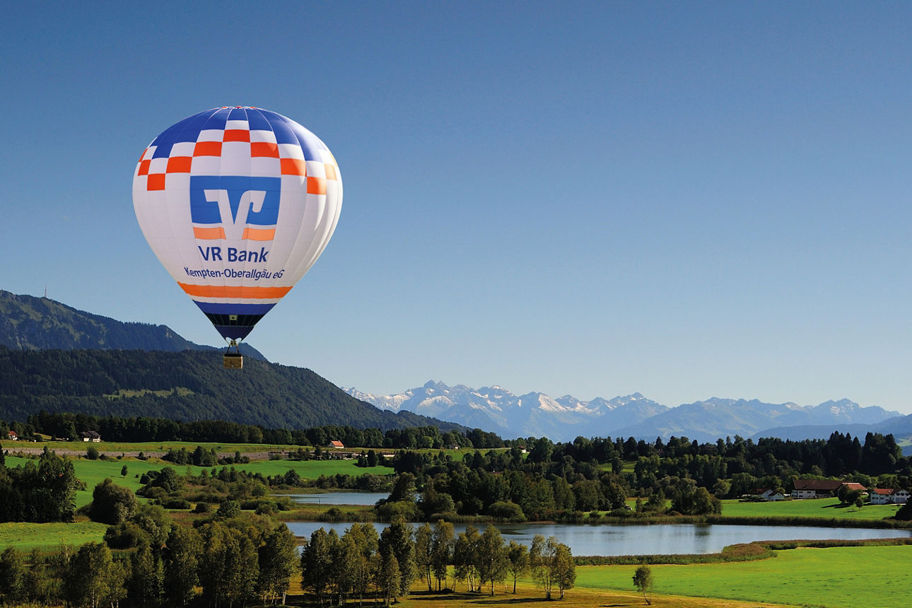 Unsere Region - Blick auf den Niedersonthofener See mit Ballon der VR Bank - im Hintergrund sind der Grünten und die Allgäuer Berge zu sehen
