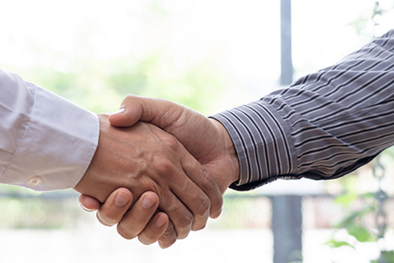 Zwei Personen schütteln sich vor einem Fenster die Hände.