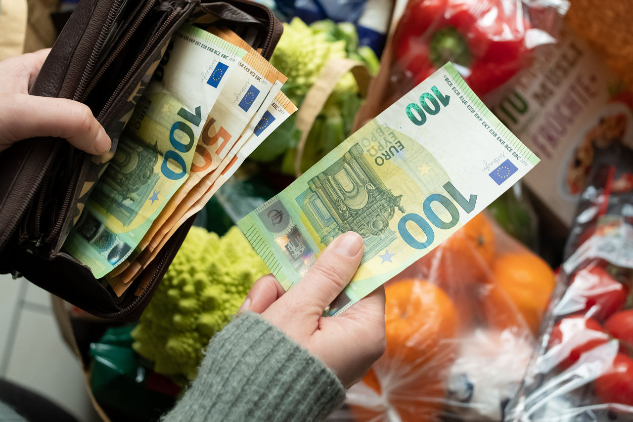 Eine Frau zieht aus einer Brieftasche mit viel Bargeld einen 100€-Schein, um ihr Einkäufe zu bezahlen