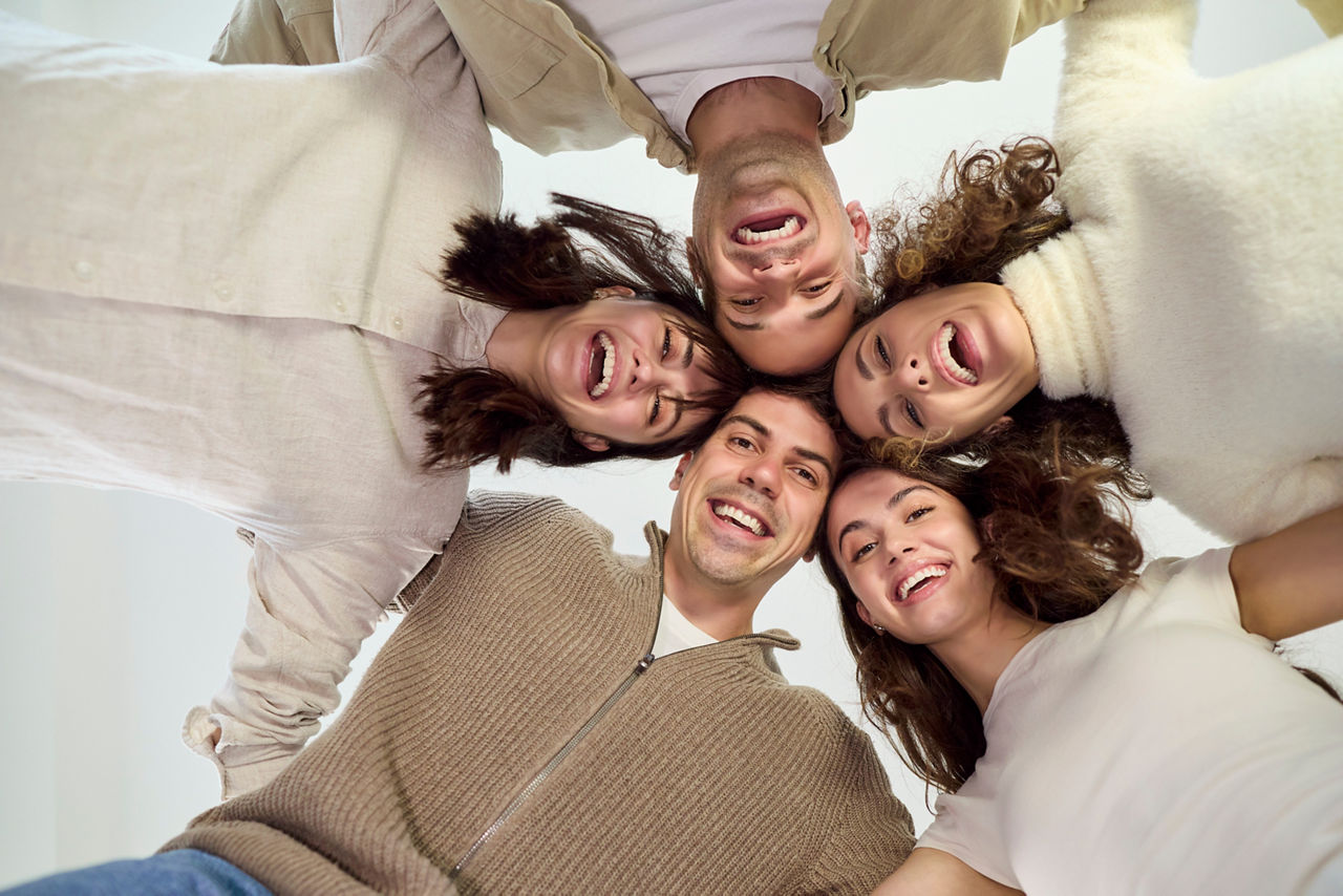 Happy young friends smiling together in group portrait. Shot from below, a playful huddle shows unity, friendship and teamwork, with laughter and support. Concept: joyful unity and friendship.