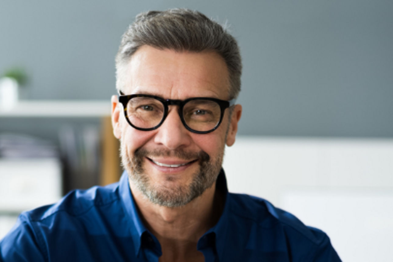 Ein Herr mit Brille sitzt an einem PC und lächelt