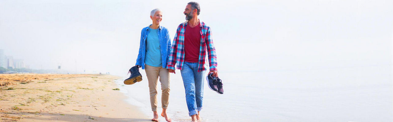 Glückliches älteres Paar geht Hand in Hand am Strand entlang